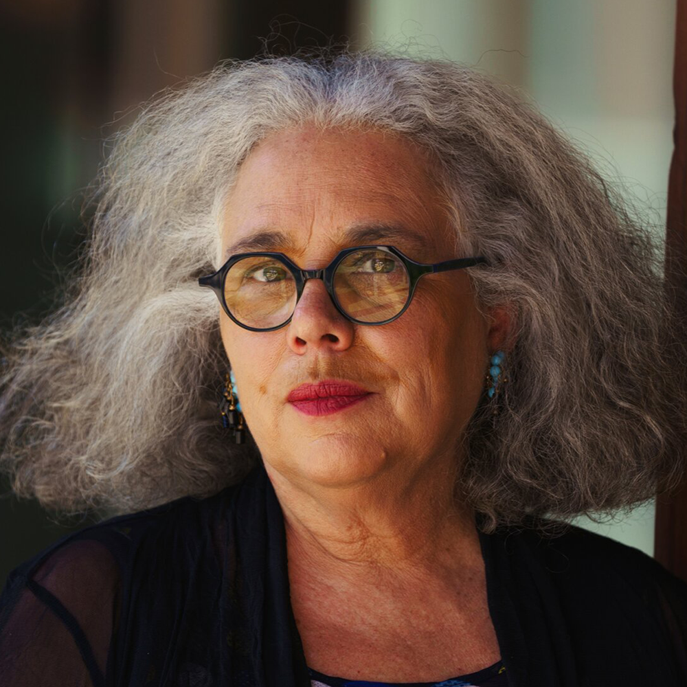 Portrait of Alison Saar, a woman with grey hair, glasses, and a black jacket