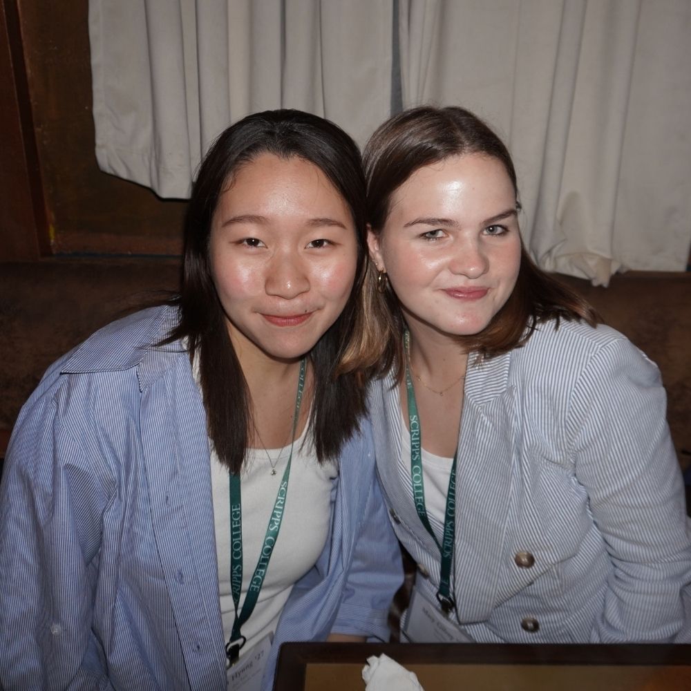 Students Jiwon Hyung, an asian woman, and Macy Gilroy, a caucasian woman, smile together at a bar