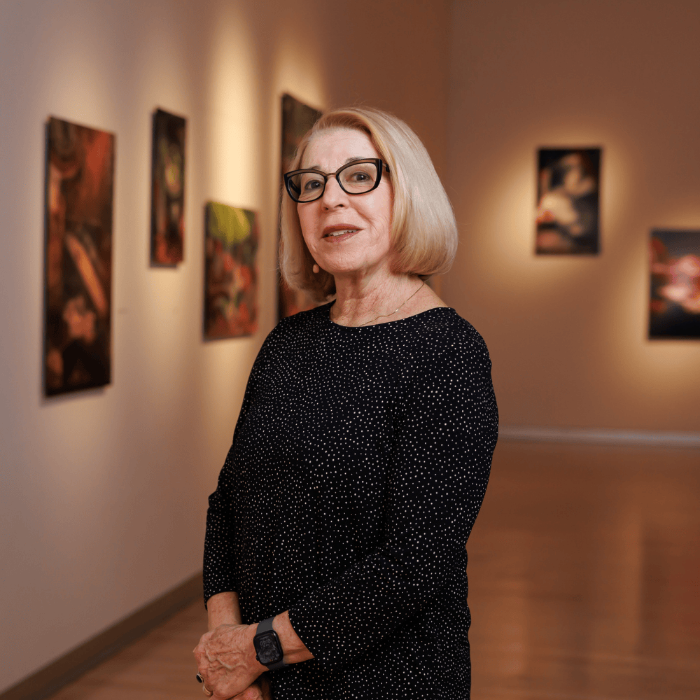 Professor of Art Nancy Macko stands in the Williamson Gallery, her photographs on display behind her.