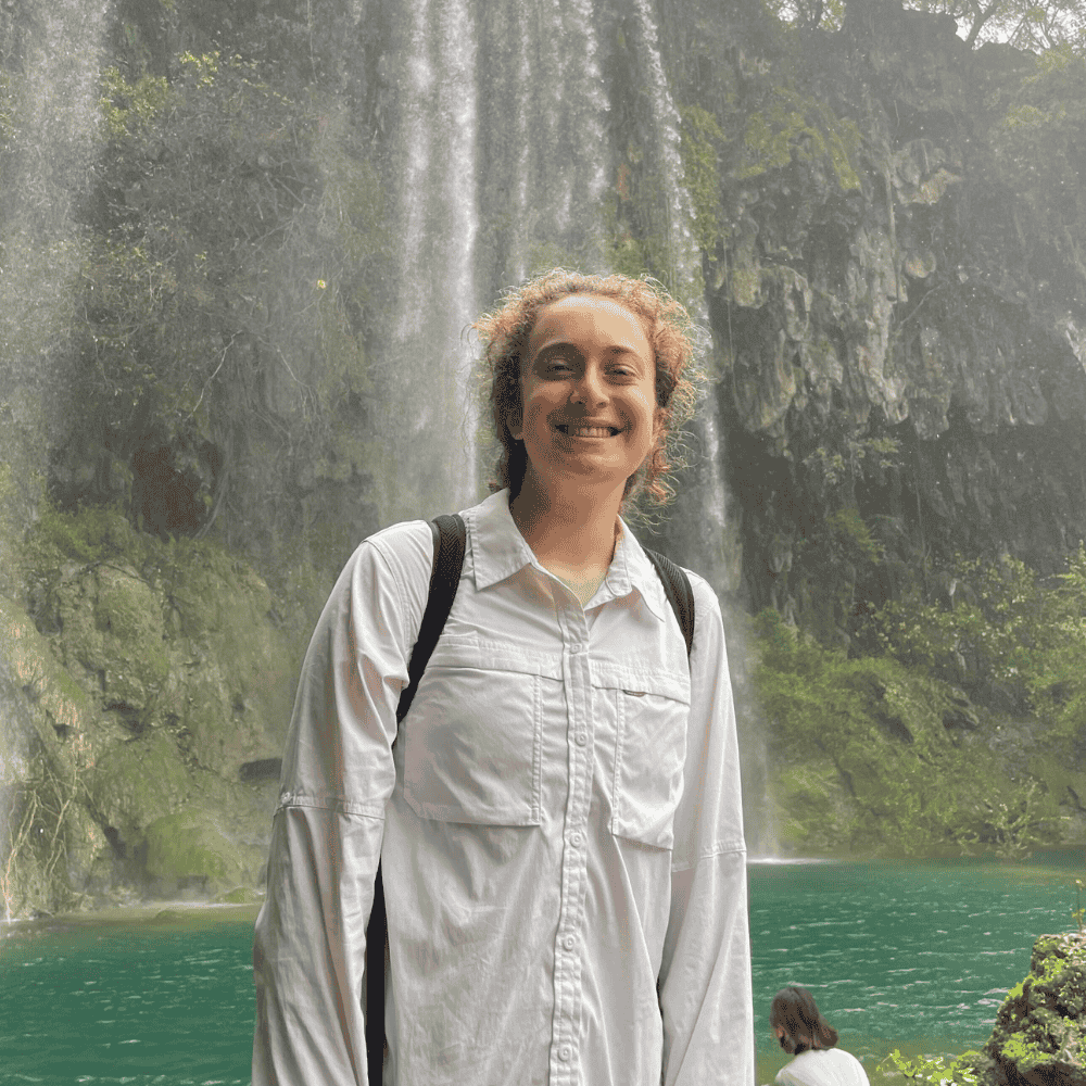 Noa Polish stands smiling in front of a waterfall in the Middle East