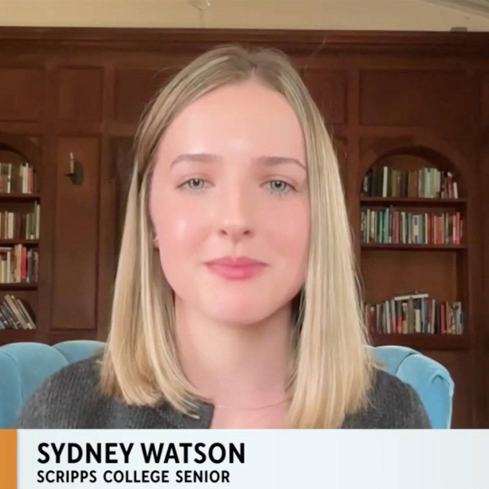 Sydney Watson, a white young woman with blonde hair and blue eyes, sits in a blue chair